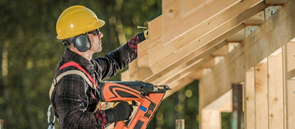 Carpenter installing timber framing using a nail gun on a construction site