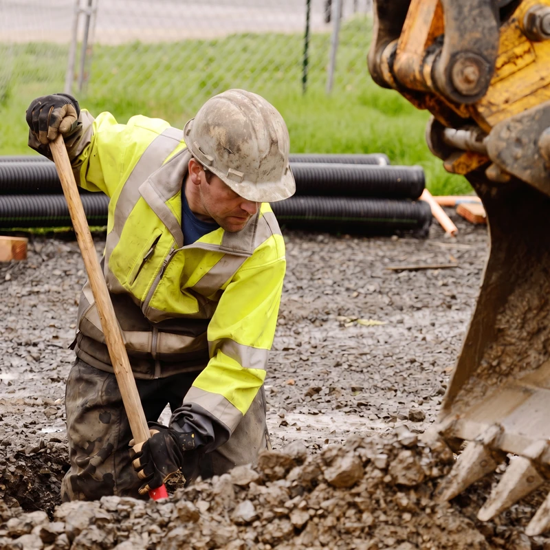Construction Worker Digging Near Excavator